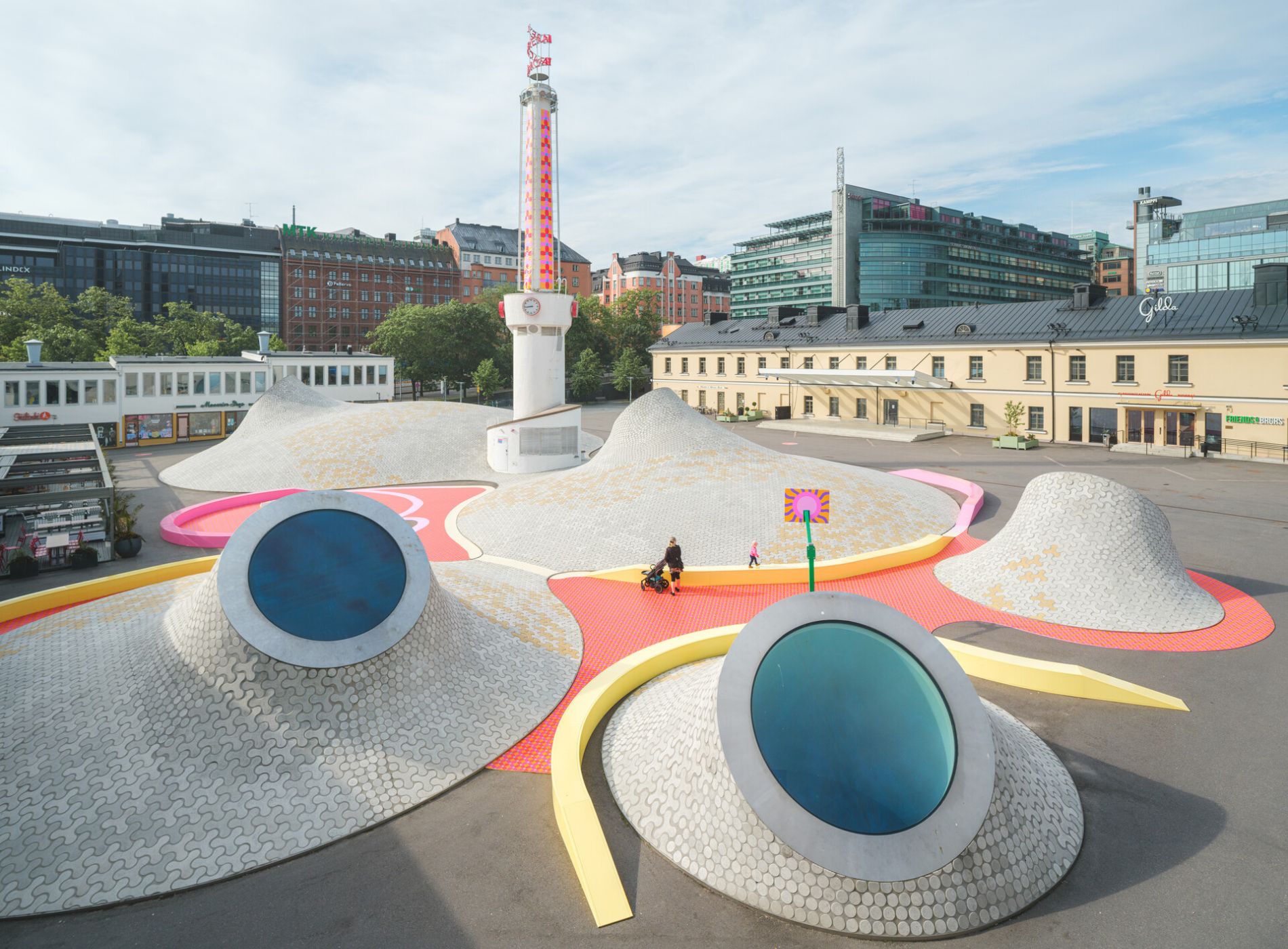 Amos Rexin kummut kohoavat Lasiapalatsinaukion keskellä. Kumpujen väliin on rakennettu Yinka Ilorin värikäs installaatio pingispöytineen ja koripallotelineineen.