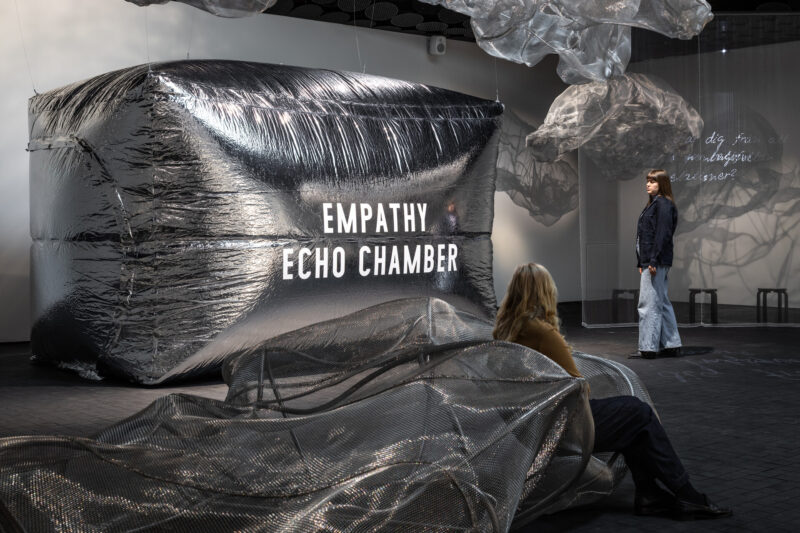 At the center of the exhibition space is a huge chamber resembling a foil balloon. Around it, both on the floor and hanging from the ceiling, are cloud-like forms and seating made of metal mesh.