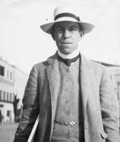 Black and white photo of Sigurd Frosterus walking on a sunny street in a three-piece suit.