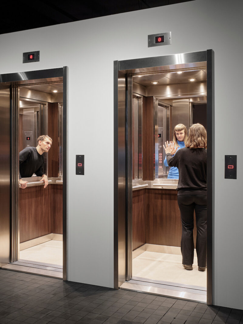 Photo showing the doorways and interiors of two elevators with people inside. The mirrors behave oddly and do not show any reflections.