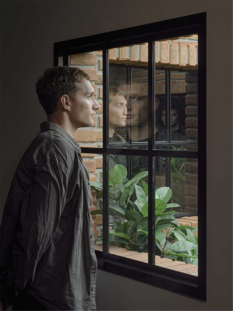 A museum visitor looks through a window into an installation filled with lush green plants.