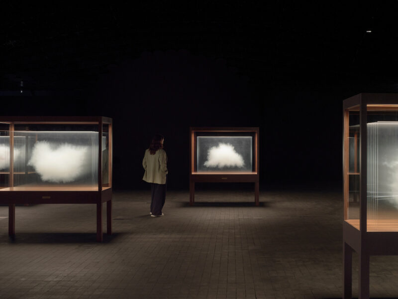 This photo shows a person walking amongst the Cloud artwork in a dark exhibition space.