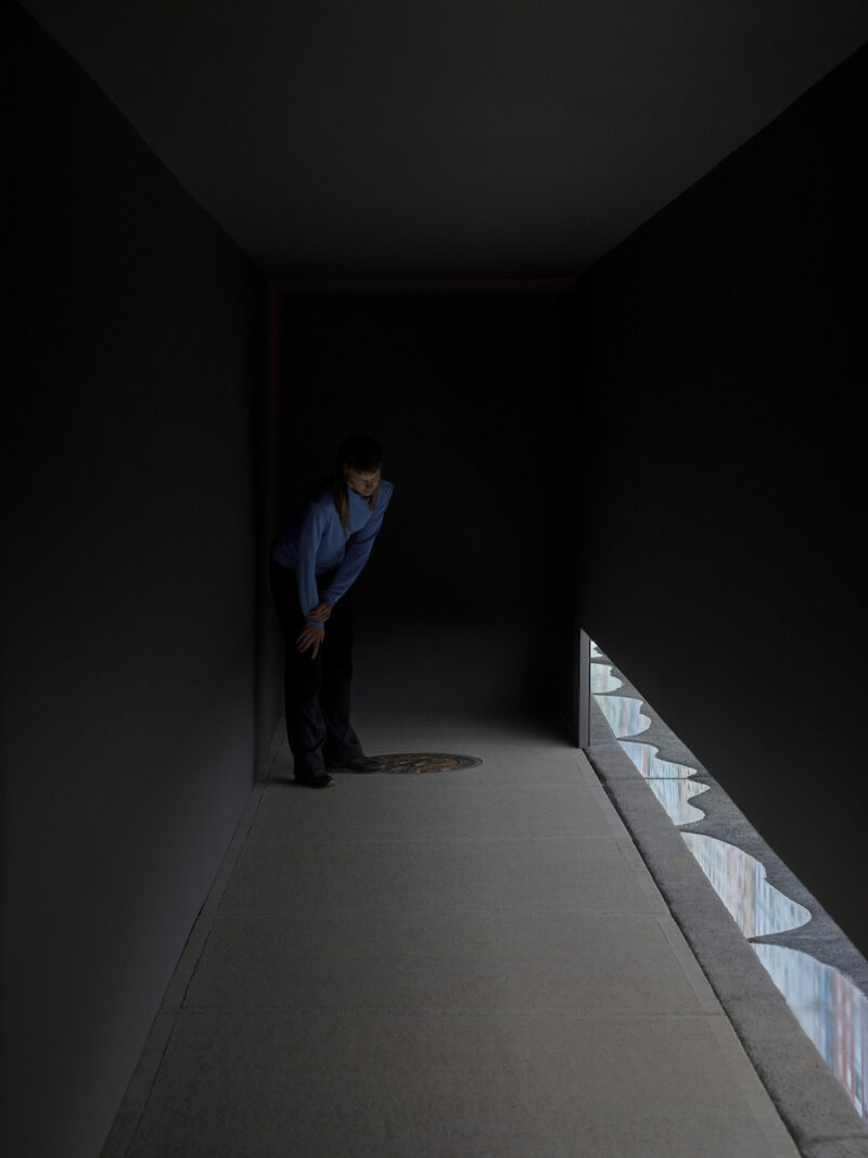 Visitor in a dark passage looking at building façades reflected in water.