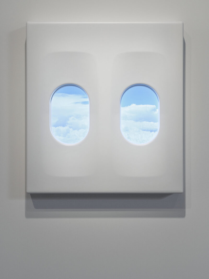 Two airplane windows show a view of clouds outside the plane.