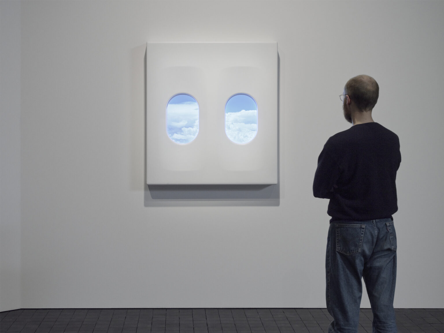 Museibesökare tittar ut genom ett flygplansfönster med blå himmel och vita moln utanför.