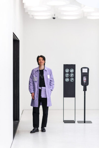Staff member in a light-violet jacket at the exhibition entrance checking admission stickers.