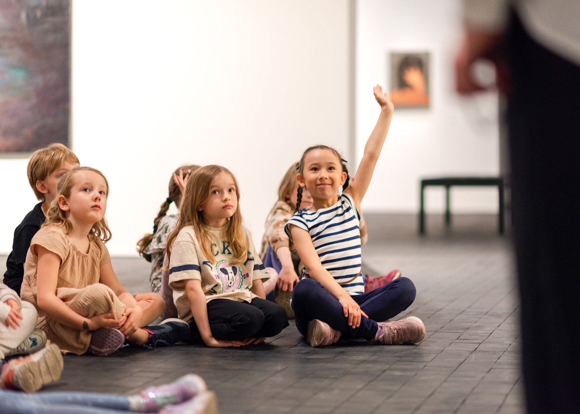 Children sitting on the floor, one child has raised their hand
