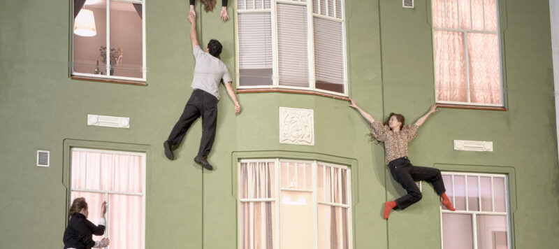 A building façade is reflected in a large mirror. People appear to be climbing on the wall due to the reflection.