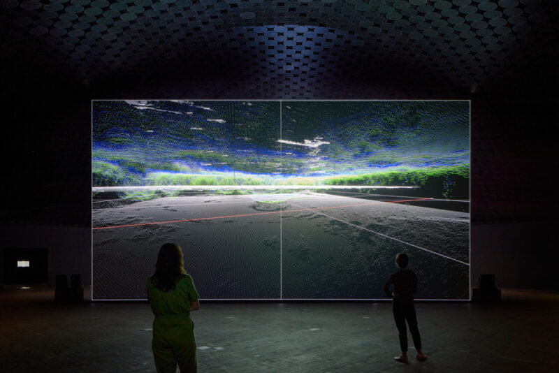 Ryoji Ikeda’s data-verse 1 on a large screen: Moving data and light, with visitors standing in front of the work.