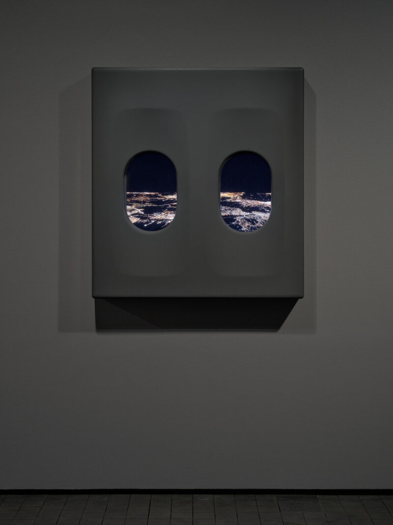 Two airplane windows. The view shows a night sky and distant city lights.
