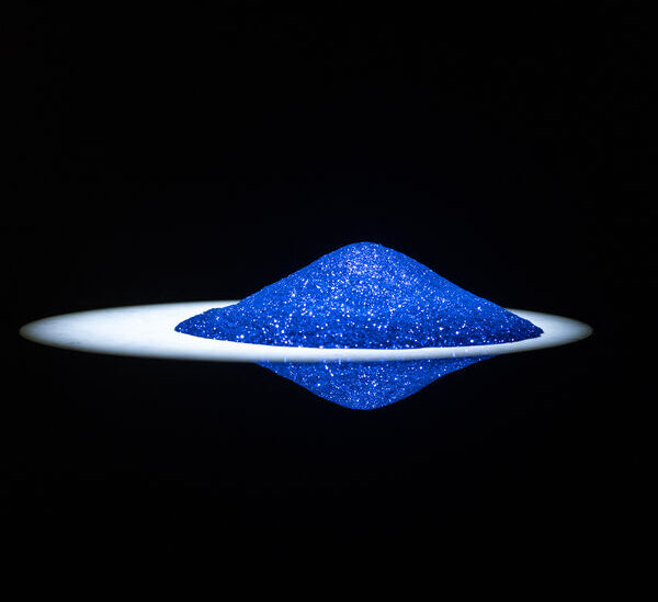 A cone-shaped pile of shimmering blue glitter dust on a dark, reflective surface.