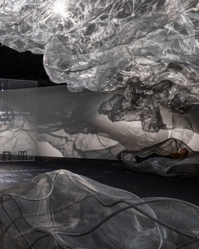 Cloud-like forms and seating made of metal mesh float and rest within the exhibition space.