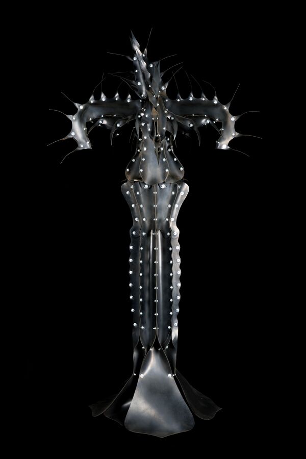 The image shows Oona Tikkaoja’s Fungus, made of black rubber and resembling a strange, cross-shaped plant or living form.