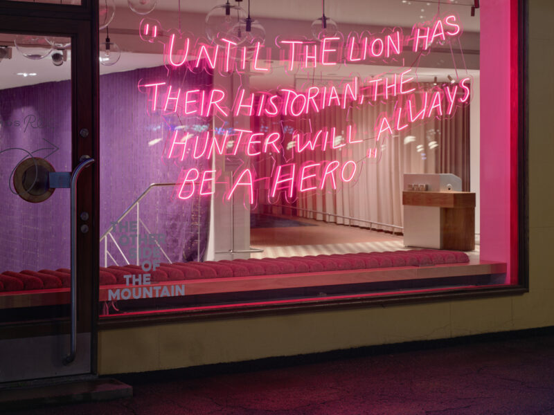 Pink neon lettering glows inside a window-like opening with stairs and curtains visible behind it.